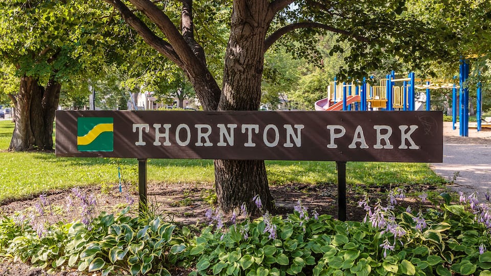A sign for Thornton Park with a tree and garden in the foreground.