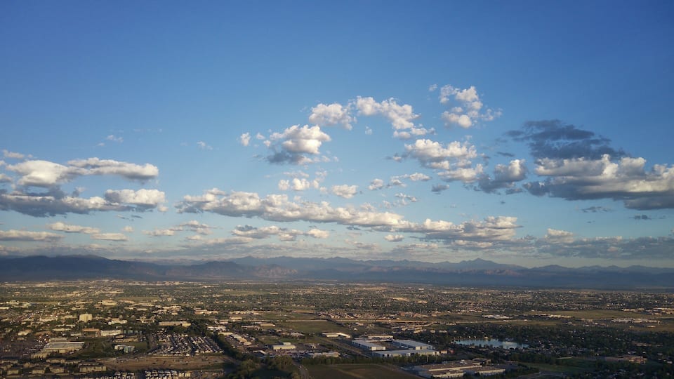 A cityscape with mountains in the background and scattered clouds in the sky.