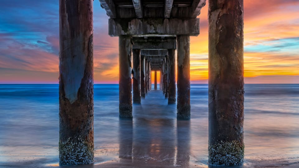 A pier extending into a calm sea at sunset.