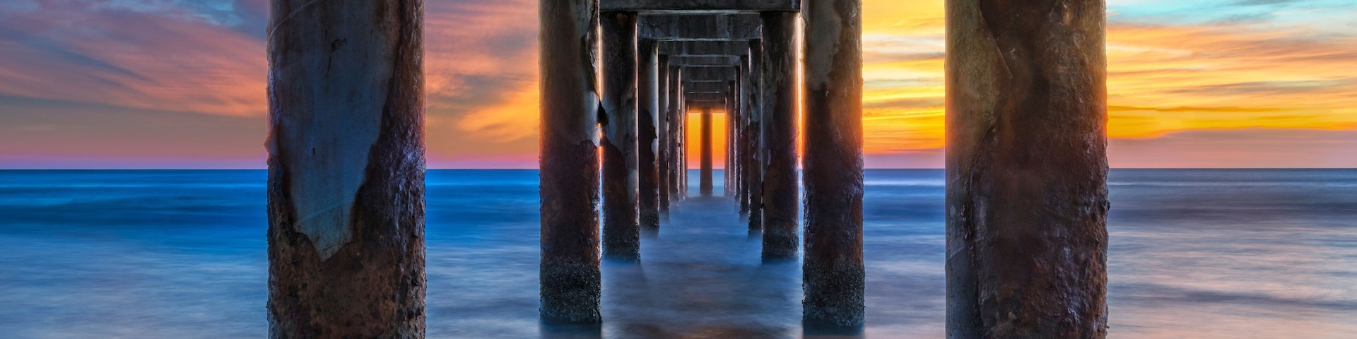 Un muelle se adentra en un mar tranquilo al atardecer.