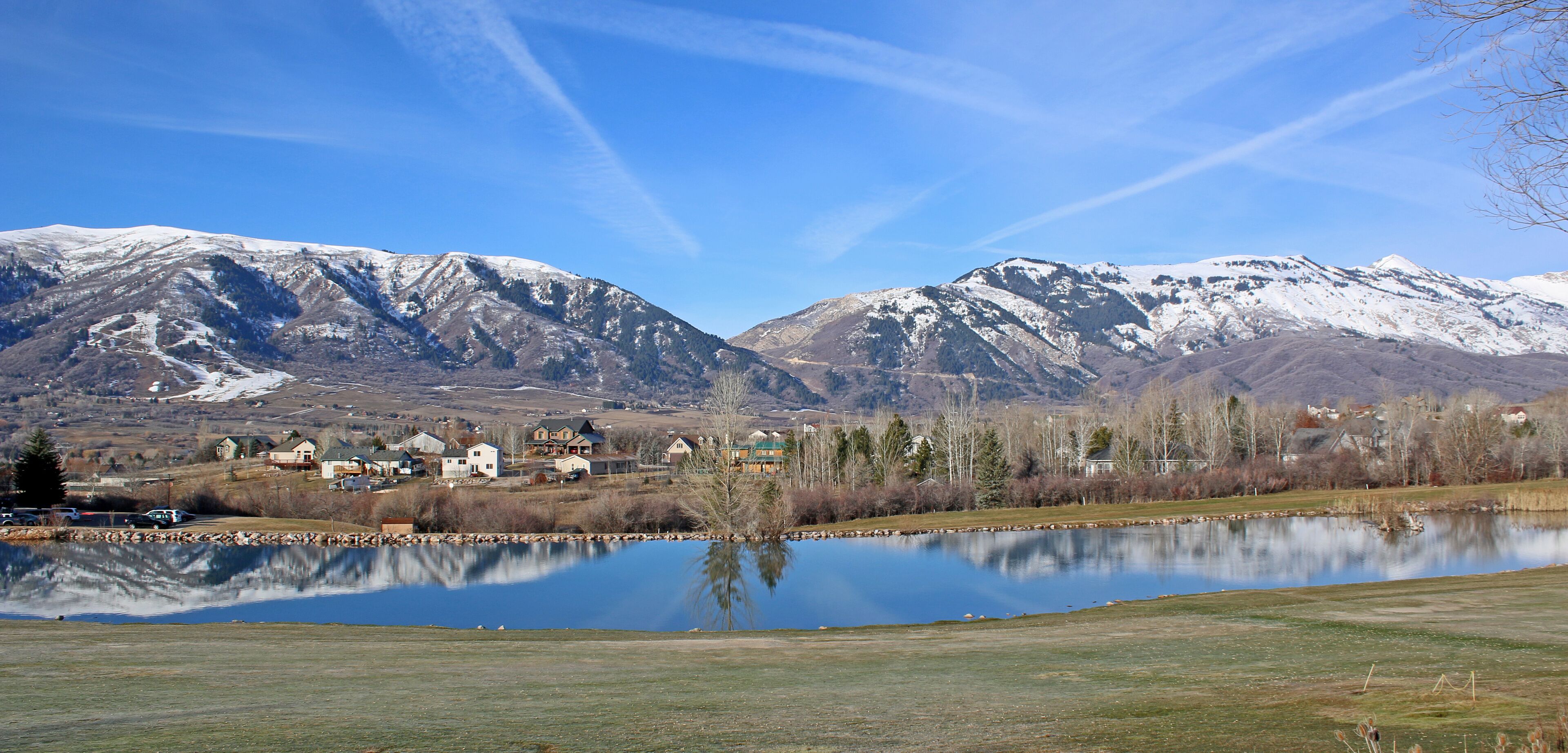 A lake reflecting snow-capped mountains, a small town with houses, and a clear blue sky.