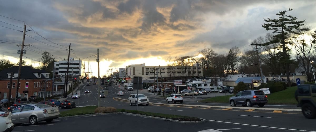 A busy intersection with cars, buildings, and a cloudy sky.