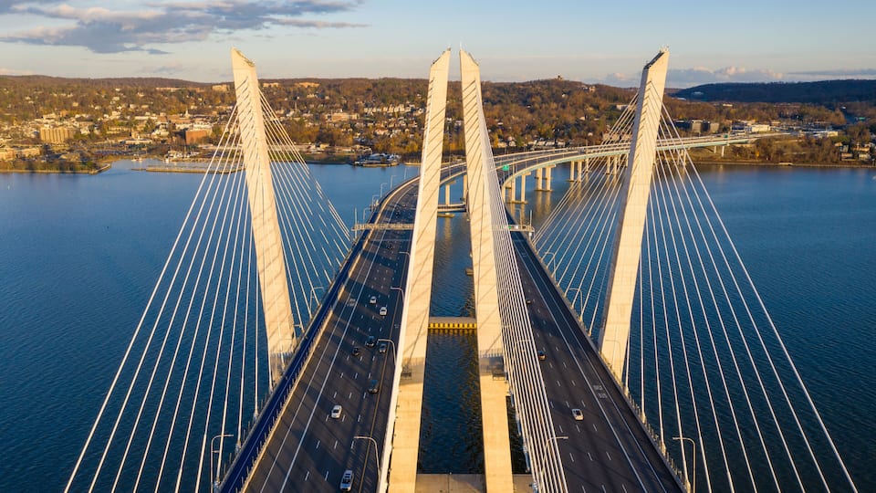 A cable-stayed bridge with multiple lanes, a river below, and a town in the background.