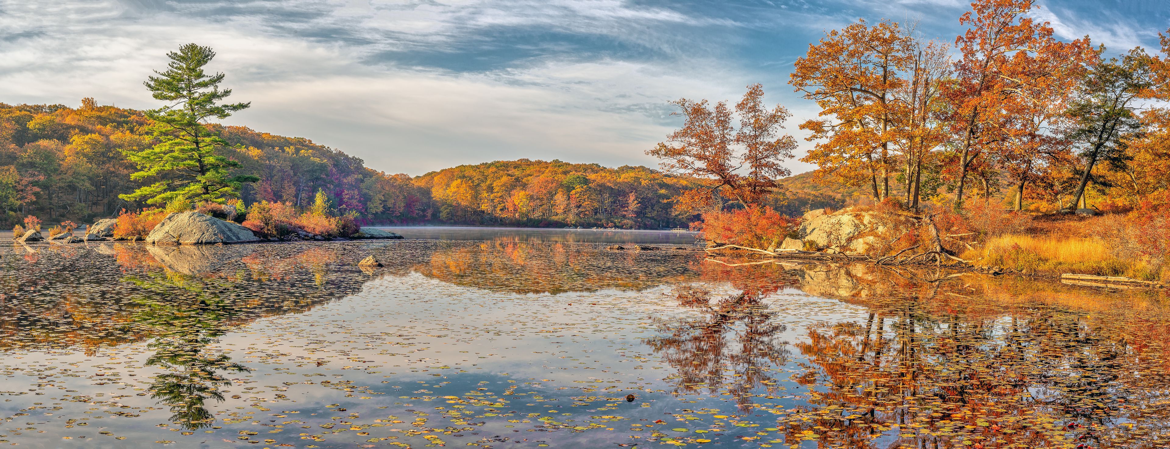 A calm lake surrounded by autumn foliage, with reflections of trees and sky on the water's surface.