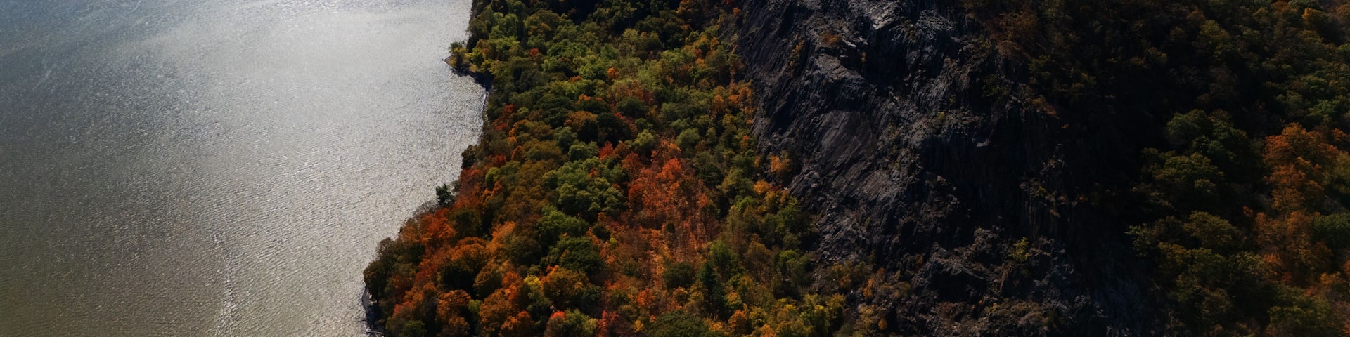 Aerial view of Hook Mountain's craggy cliffs meet the Hudson River under a vast sky, autumn foliage ablaze in fiery hues near the Tappan Zee Bridge., Nyack, New York, United States.