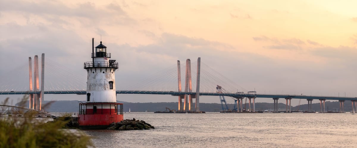 Panorama of a caisson (sparkplug) style lighthouse under soft golden light with a bridge in the background. Tarrytown Light on the Hudson River in New York.