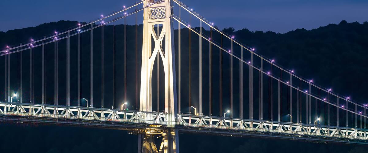 A large suspension bridge at night with illuminated cables and a central tower.