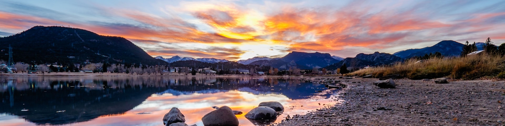 A sunset over a calm lake with mountains in the background and a rocky shoreline.