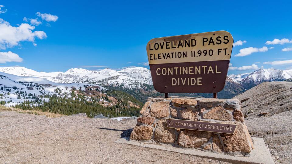 A sign indicating the Loveland Pass elevation at 11,990 feet and the Continental Divide, with a U.S. Department of Agriculture label.