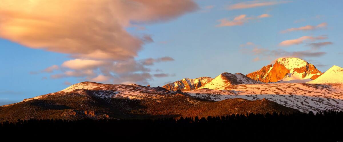 A mountain range with snow-capped peaks and a forested foreground.