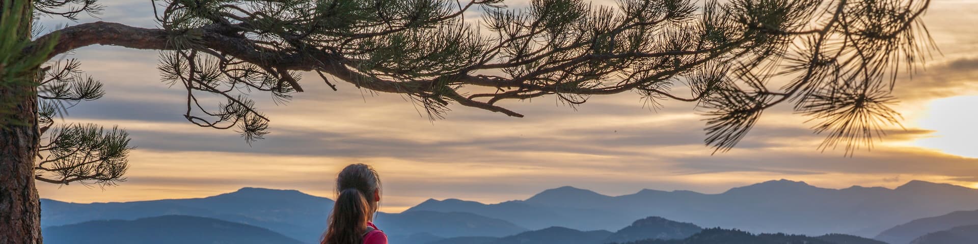 A hispanic woman is hiking with a dog, at sunset, in the Rocky Mountains near Denver, Colorado, USA