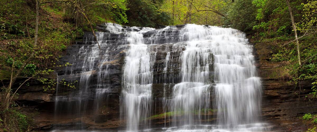 A multi-tiered waterfall surrounded by dense forest.
