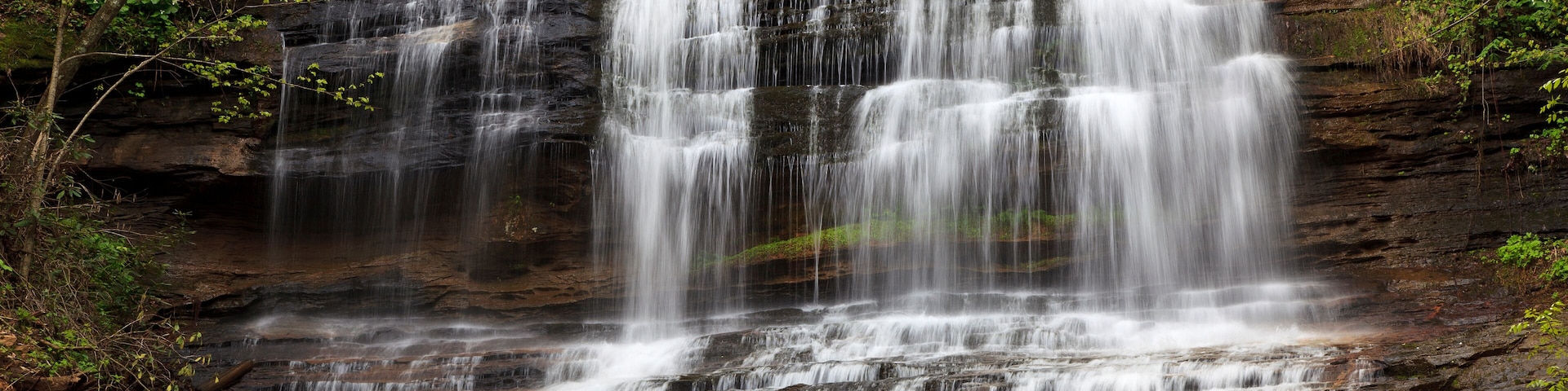 A multi-tiered waterfall surrounded by dense forest.