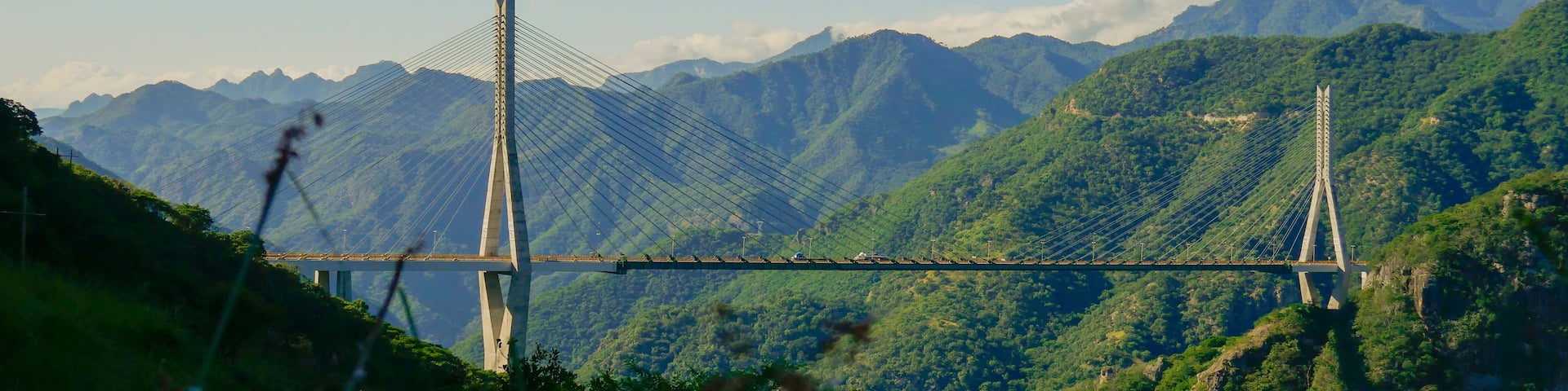 A cable-stayed bridge spanning a lush valley with mountains in the background.