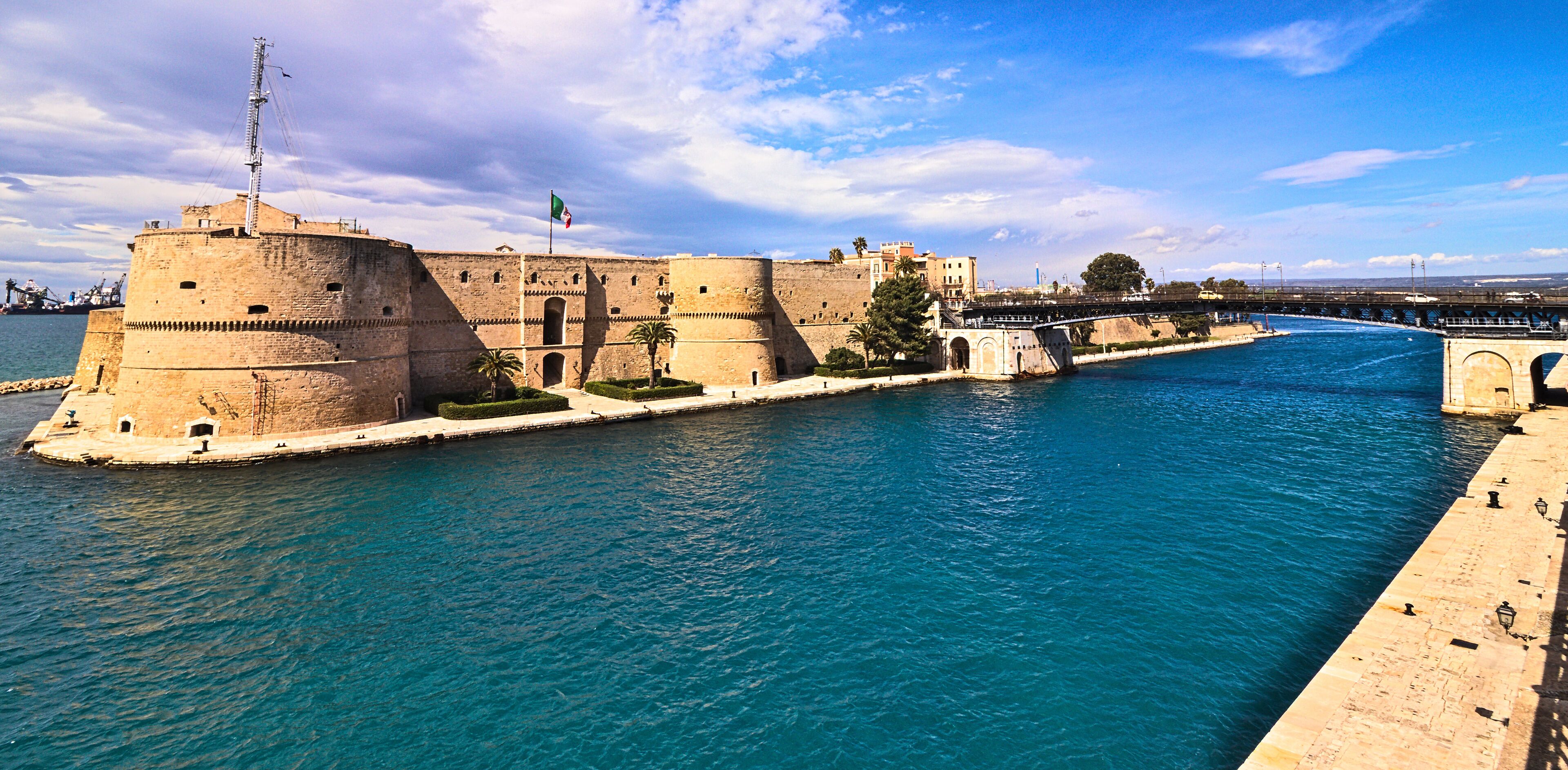 A historic fortification by a river with a bridge in the background.