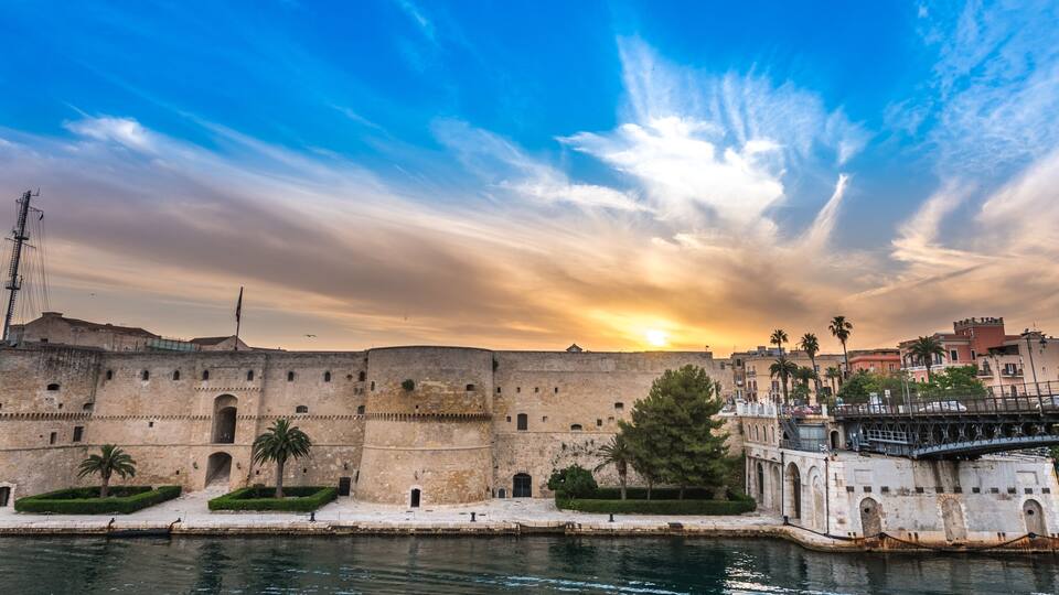 A historic fortification by a river with a sunset in the background.