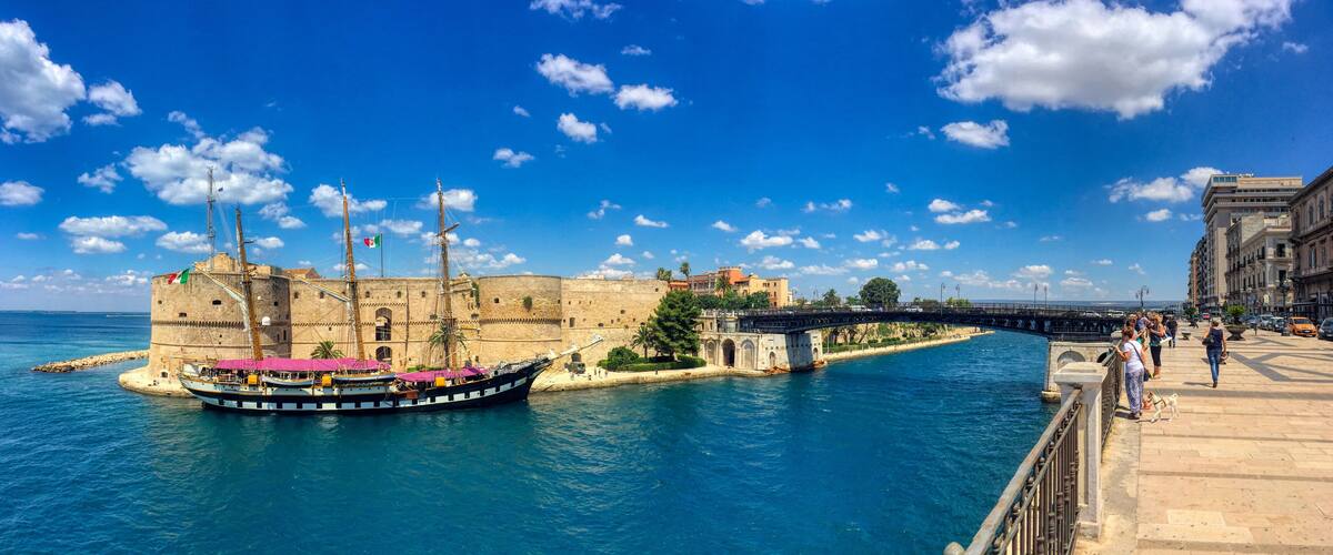 Eine historische Festung, ein großes Segelschiff im Hafen und eine Brücke, die zwei Landstriche verbindet.