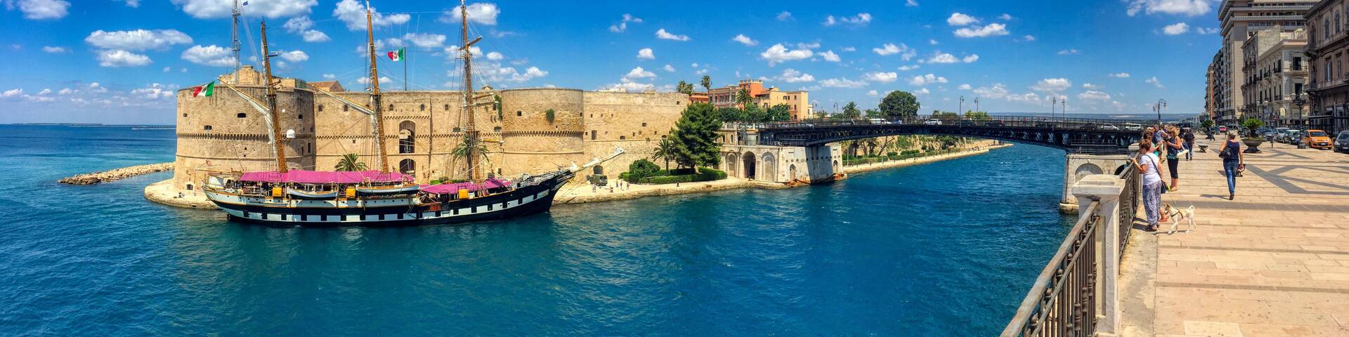 A historic fort, a large sailing ship docked at the harbor, and a bridge connecting two land masses.
