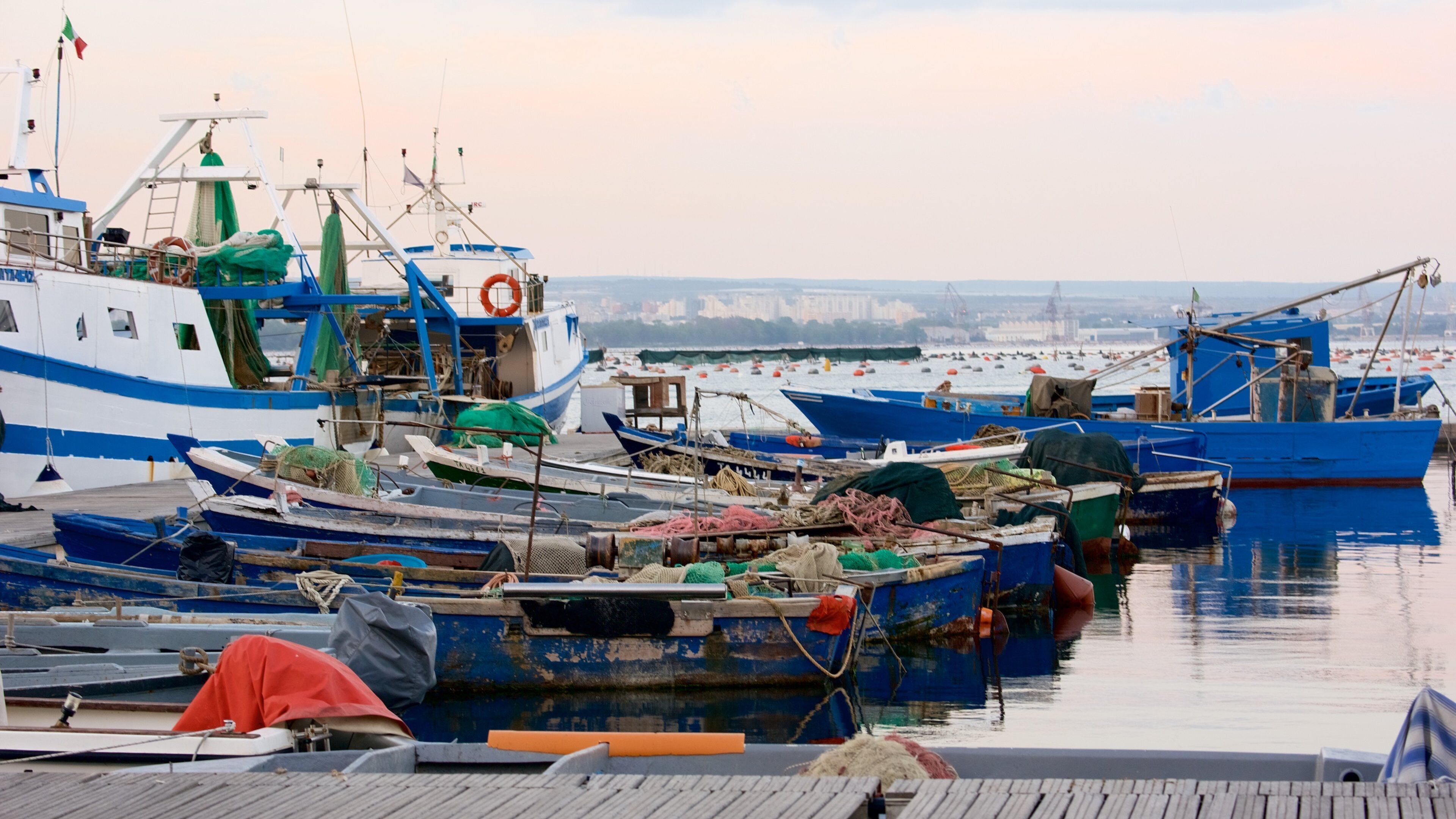 A harbor with multiple fishing boats docked, some with nets and equipment on deck.