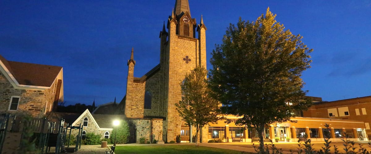 A church with a tall spire and a clock tower at dusk.