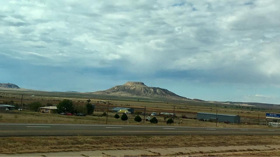 A highway with a mountain in the distance, a few buildings, and a cloudy sky.