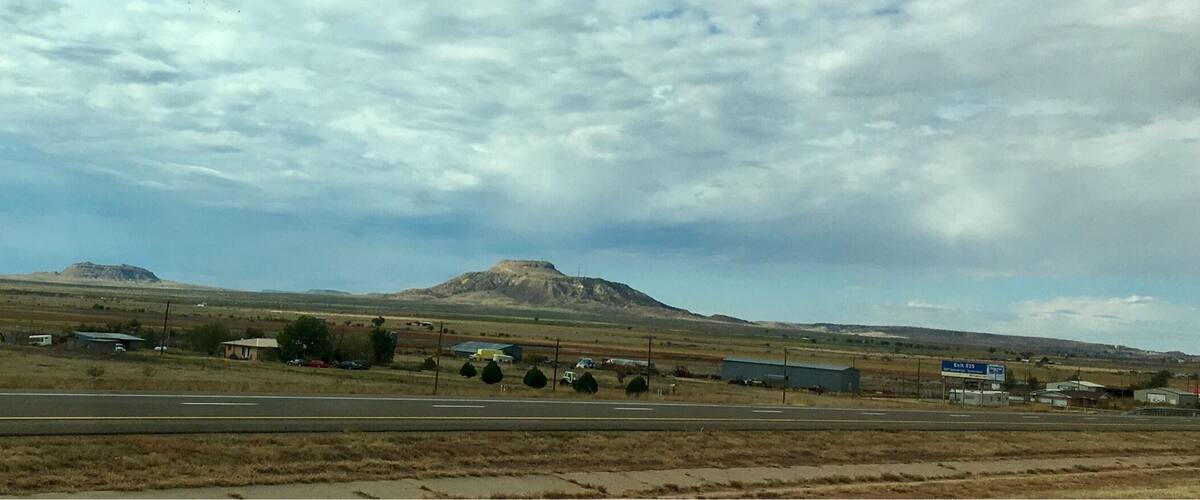 A highway with a mountain in the distance, a few buildings, and a cloudy sky.