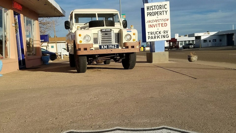 A vintage Land Rover parked in front of the Blue Swallow Motel, with a sign indicating historic property inspection and truck & RV parking.