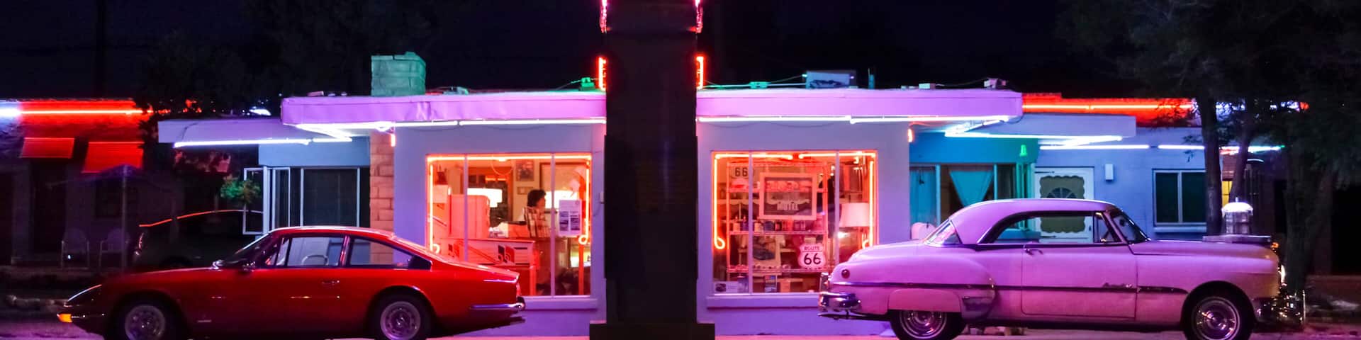 Tucumcari, New Mexico, USA. Famous Blue Swallow Motel on Route 66 at twilight with old cars parked in front and neon sign brightly lit. Property released