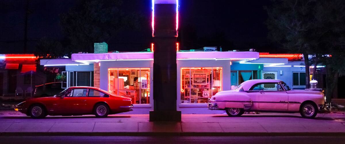 A vintage car in front of a brightly lit building with neon signs.