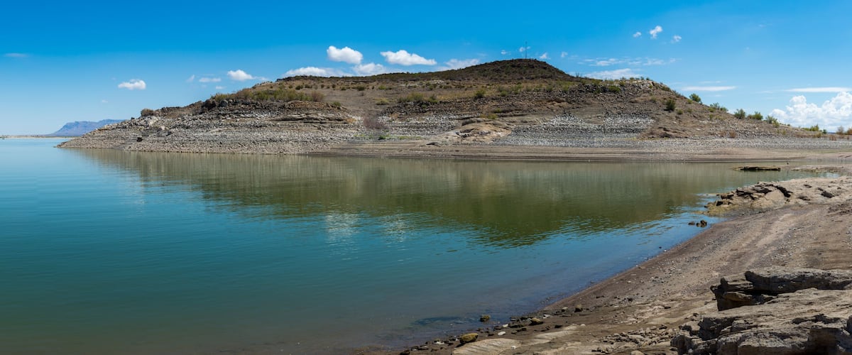 A calm lake with a rocky shoreline and a hill in the background.