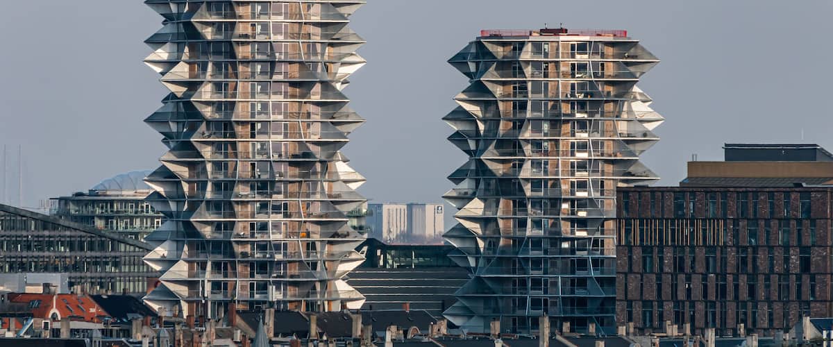 Dos edificios altos de diseño singular con un patrón en zigzag, frente a un paisaje urbano.