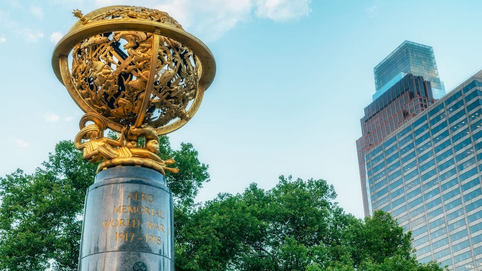 A golden memorial with inscriptions, set against a backdrop of modern buildings and trees.