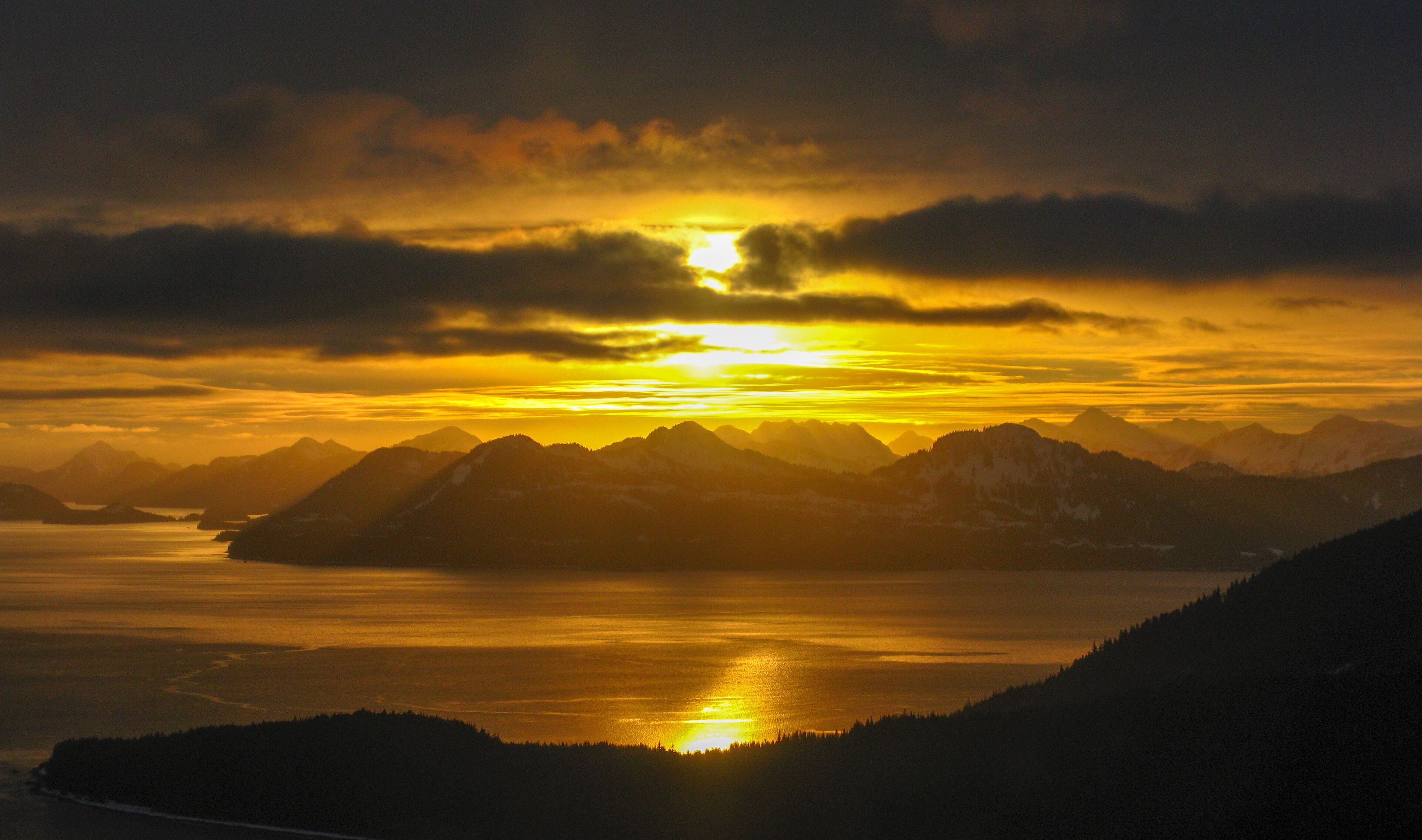 A sunset over a mountainous landscape with a body of water in the foreground.