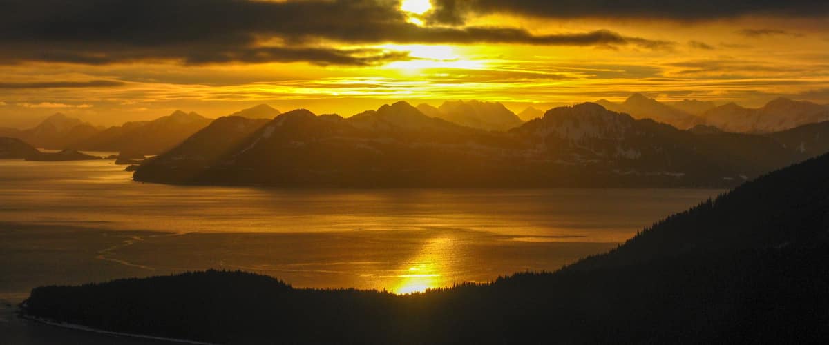 A sunset over a mountainous landscape with a body of water in the foreground.