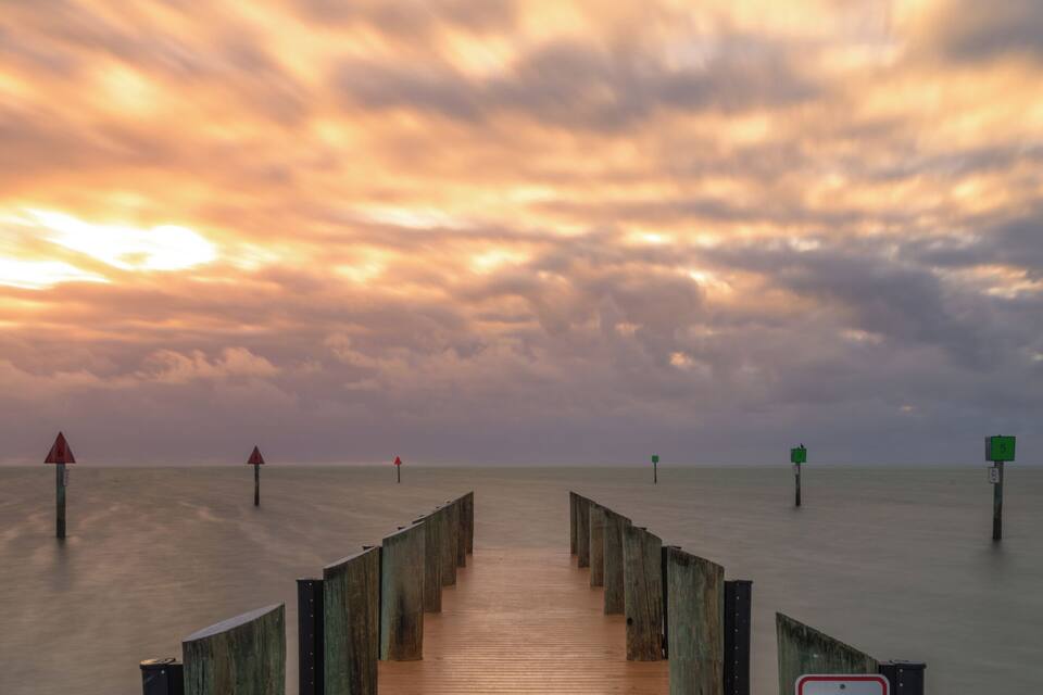 A wooden pier leading into calm waters with a sunset sky.