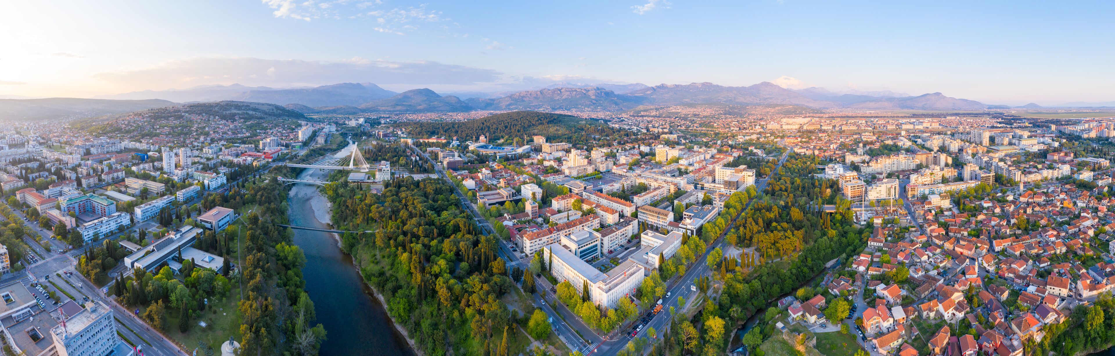 A panoramic view of a city with a river, bridges, and mountains in the background.