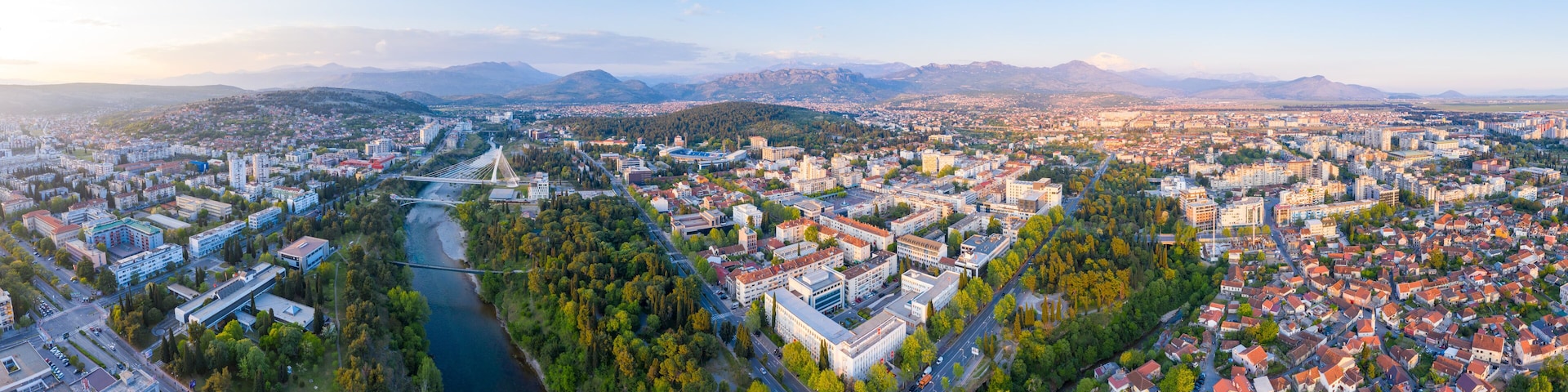 A panoramic view of a city with a river, bridges, and mountains in the background.