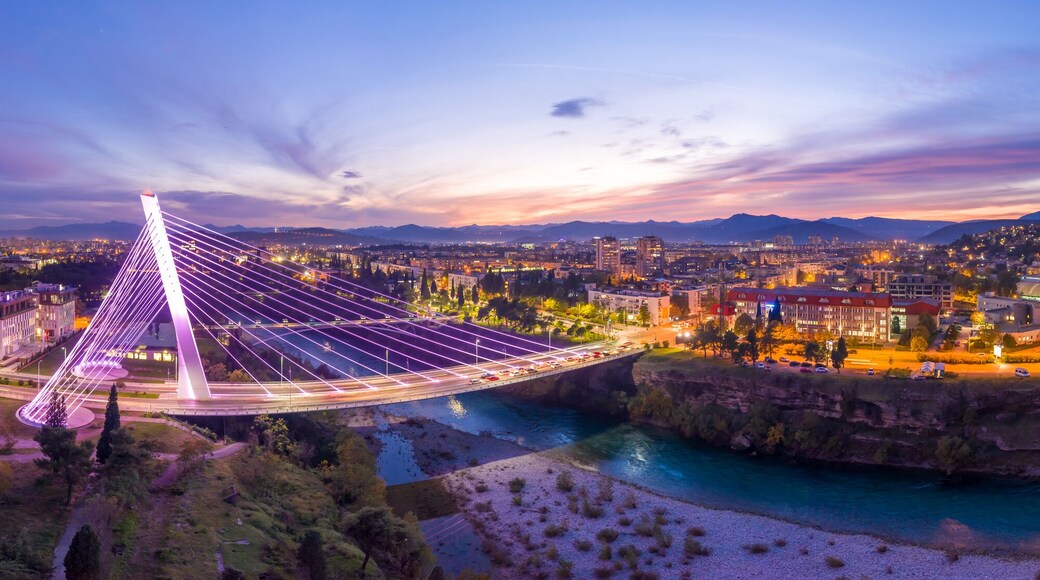 Illuminated Millennium bridge over Moraca river in Podgorica Montenegro, at night. 180 degrees panorama of the city under sunset sky with moon in it.