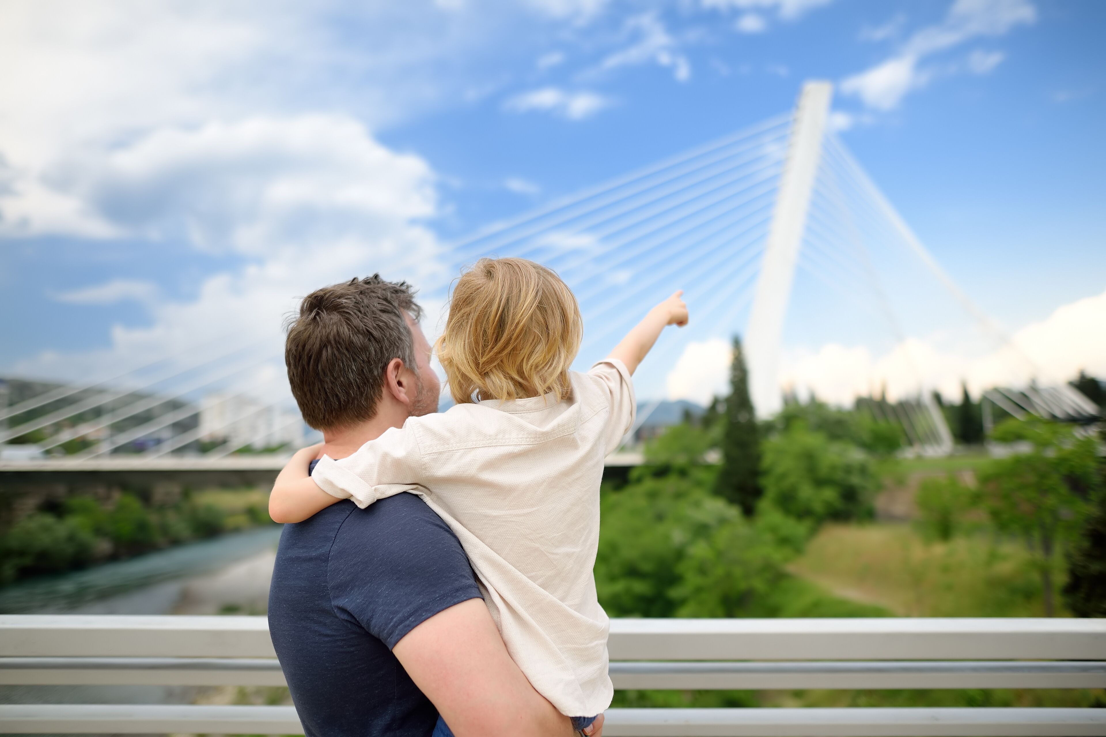Little child and middle age father are admiring of cable stayed bridge. Boy is pointing of hand on Millennium bridge is above Moraca river in Podgorica, Montenegro.