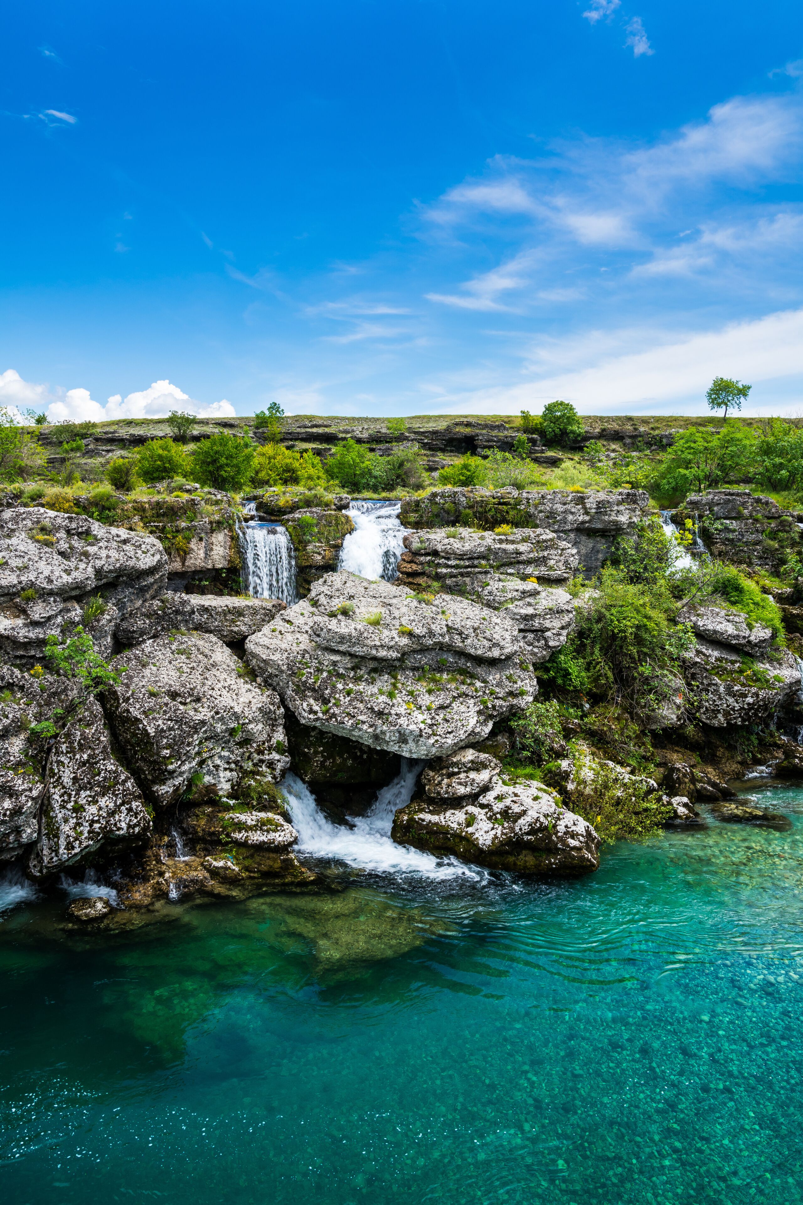 Una cascada que se precipita sobre terreno rocoso, con agua turquesa cristalina abajo.