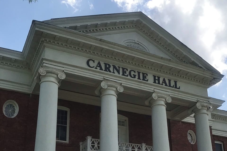 Fachada del Carnegie Hall con columnas y el nombre 'CARNEGIE HALL' en la parte superior.