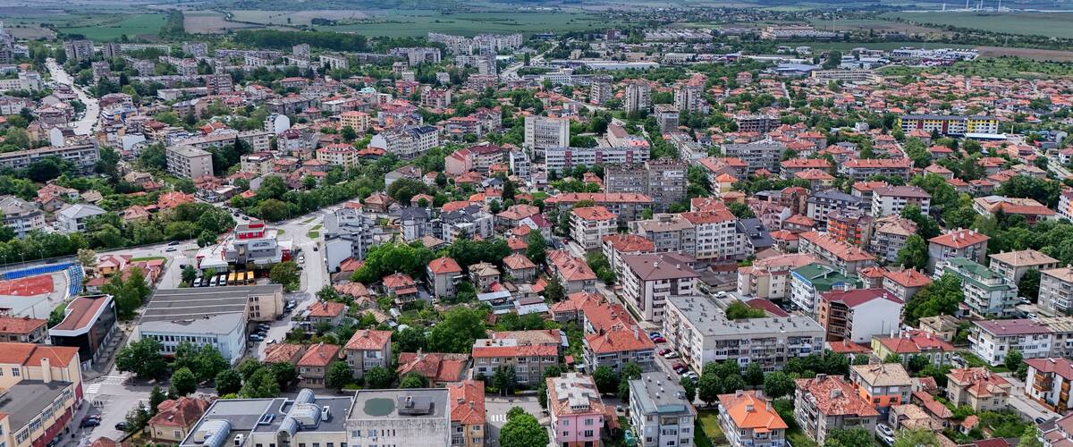 A densely populated urban area with a mix of residential and commercial buildings, surrounded by green hills and a cloudy sky.