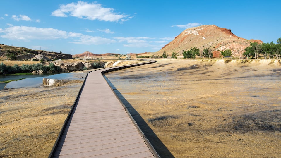 A boardwalk along a riverbank with a mountainous backdrop.