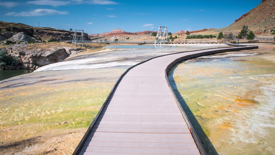 A curved wooden bridge over a river with a rocky landscape and a clear sky.
