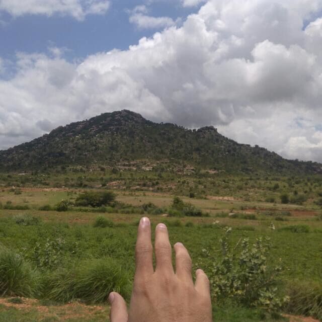 A hand in the foreground with a mountainous landscape in the background.