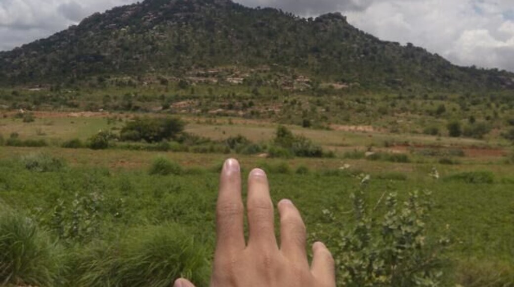 A hand in the foreground with a mountainous landscape in the background.