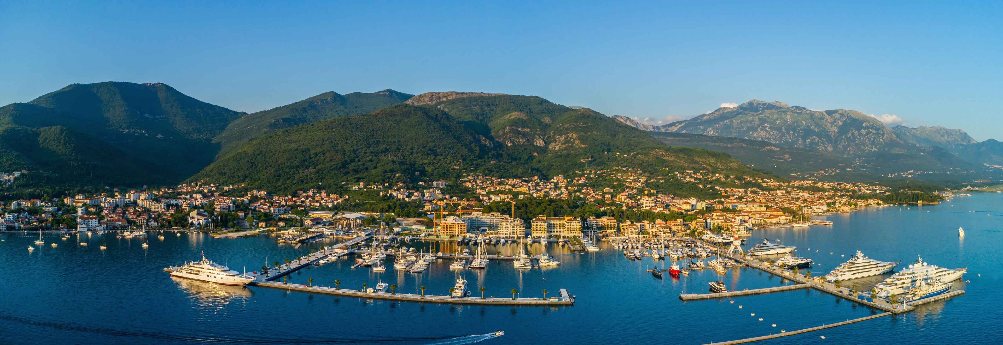 A coastal town with a marina, boats, and mountains in the background.