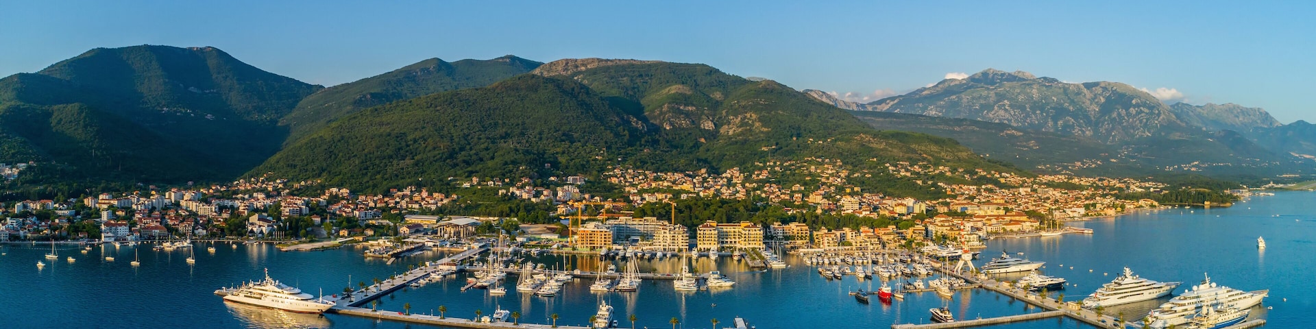 A coastal town with a marina, boats, and mountains in the background.