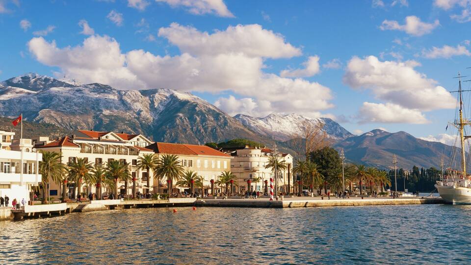 Sunny winter in Mediterranean town. Panoramic view of the embankment of Tivat city and snow-capped Lovcen mountain, Montenegro