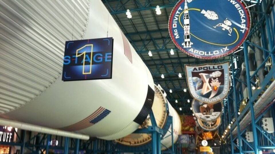 A space shuttle interior with NASA logos and a crowd of visitors.
